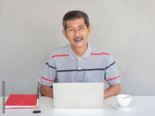 Asian businessman, seniors enjoy using laptops on a white table. With a pen and a red book.He is studying the use of modern technology.