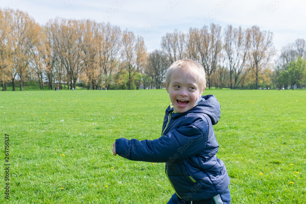 Defect,childcare,medicine and people concept: Blond boy with down syndrome playing in a park at spring time. Defect,childcare,medicine and people concept: Blond boy with down syndrome playing in a park at spring time.