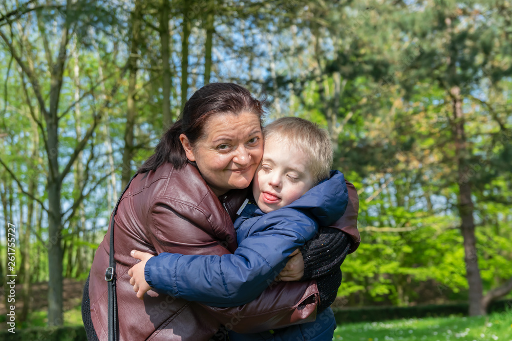 Defect,childcare,medicine and people concept: Happy mother and son with down syndrome playing together in a park at spring time. Defect,childcare,medicine and people concept: Happy mother and son with down syndrome playing together in a park at spring time.
