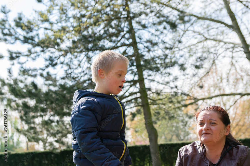 Defect,childcare,medicine and people concept: Happy mother and son with down syndrome playing together in a park at spring time. Defect,childcare,medicine and people concept: Happy mother and son with down syndrome playing together in a park at spring time.