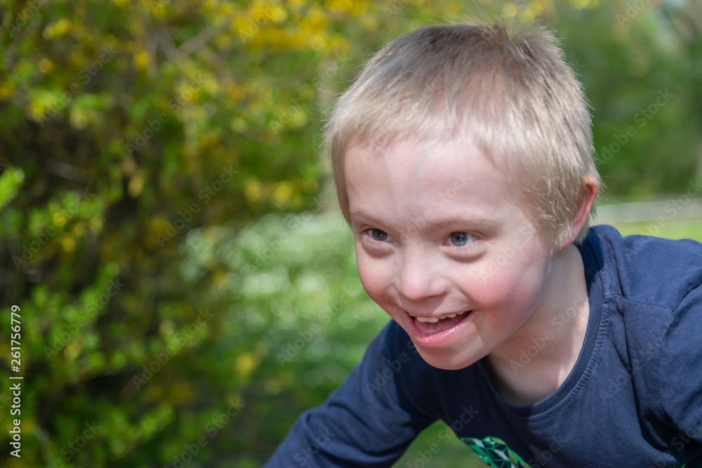 Defect,childcare,medicine and people concept: Blond boy with down syndrome playing in a park at spring time. Defect,childcare,medicine and people concept: Blond boy with down syndrome playing in a park at spring time.