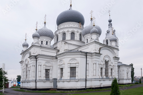 Christian orthodox white church with silver and grey domes with gold crosses. Calm grey sky above