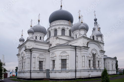 Christian orthodox white church with silver and grey domes with gold crosses. Calm grey sky above © Oksana