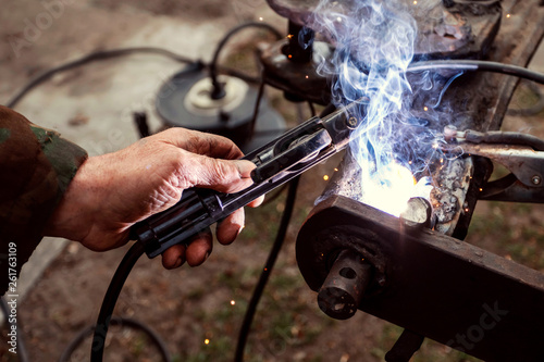 Close up industrial worker is welding repair auto in factory. Mechanical engineering, agricultural technology, garage concept.