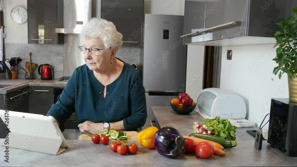 happy senior active woman cooking at home in modern kitchen and looking for recipe on a internet computer tablet happy senior active woman cooking at home in modern kitchen and looking for recipe on a internet computer tablet