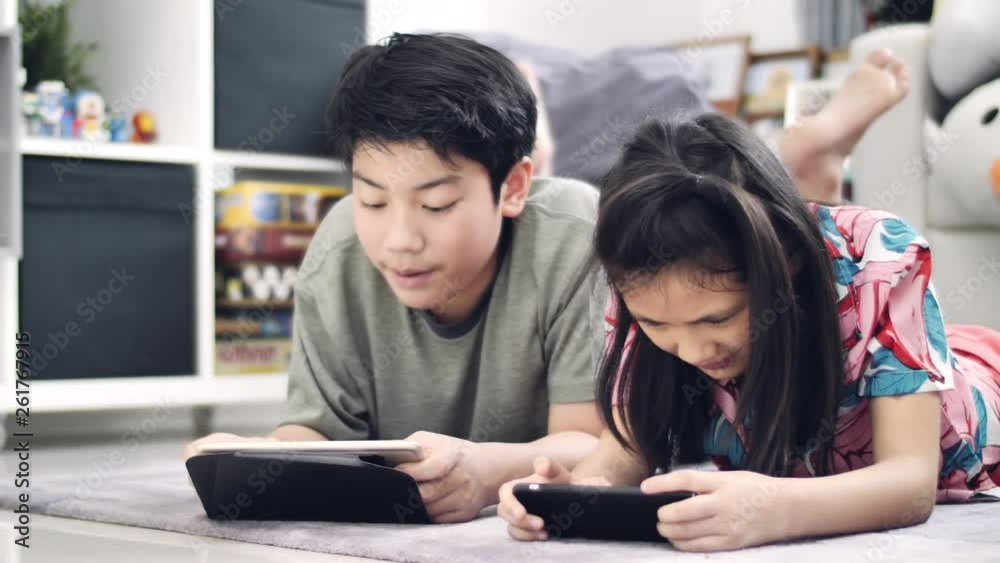 Children playing tablet or smartphone at home , Asian boy and girl playing game on mobile phone together with smile face. Children playing tablet or smartphone at home , Asian boy and girl playing game on mobile phone together with smile face.