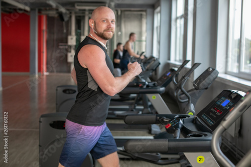 Canadian Fit Muscle bald Man With Headphones Running on Treadmill in Gym.