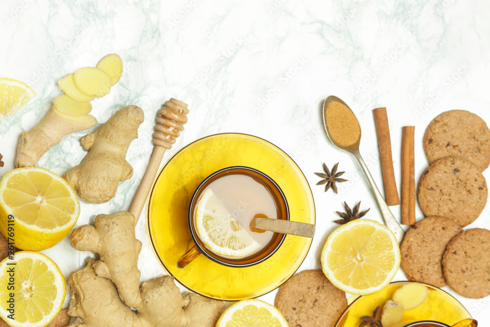 Ginger tea in a cup with ginger roots and lemon on marble textured background, top view. A healthy lifestyle, anti-flu and anti-inflammatory concept. Ginger tea in a cup with ginger roots and lemon on marble textured background, top view. A healthy lifestyle, anti-flu and anti-inflammatory concept.