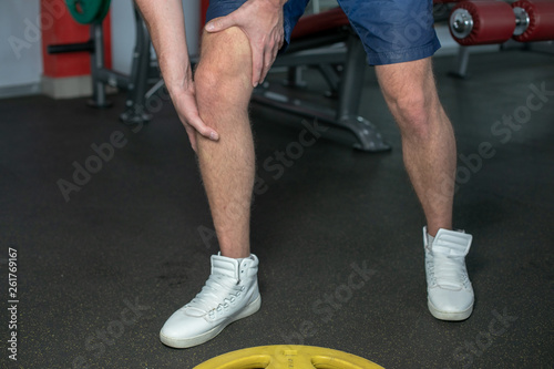Sportsman in white sneakers and blue jeans having pain in leg after exercise in gym. close up. focus is on leg.