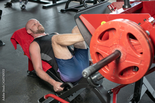 Side view of bald man in black t-shirt weightlifter doing leg presses in gym