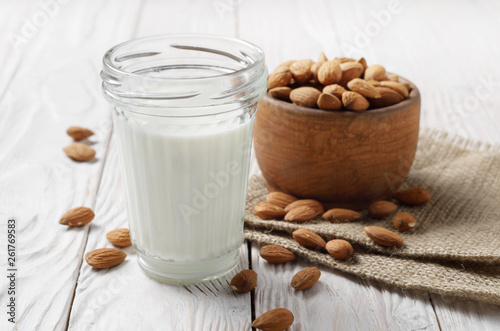 Milk or yogurt in mason jar on white wooden table with bowl of almonds on hemp napkin aside