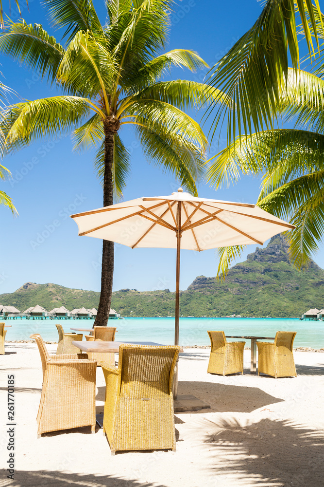 Chairs and coffee table under a thatched parasol on a sand beach with a view on the lagoon