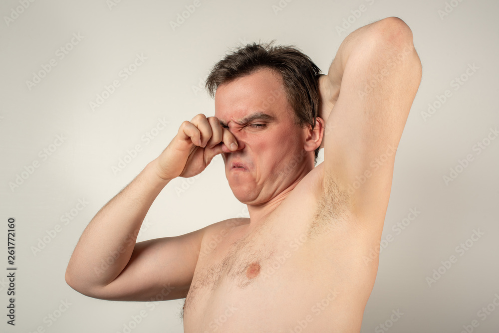 A man with smelly armpits holds his nose with his hand on a white background A man with smelly armpits holds his nose with his hand on a white background