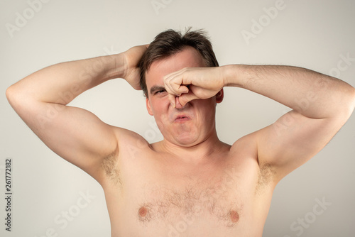 A man with smelly armpits holds his nose with his hand on a white background