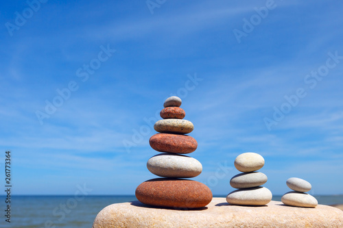 Three Zen pyramid of balanced stones on a background of the summer sea and blue sky