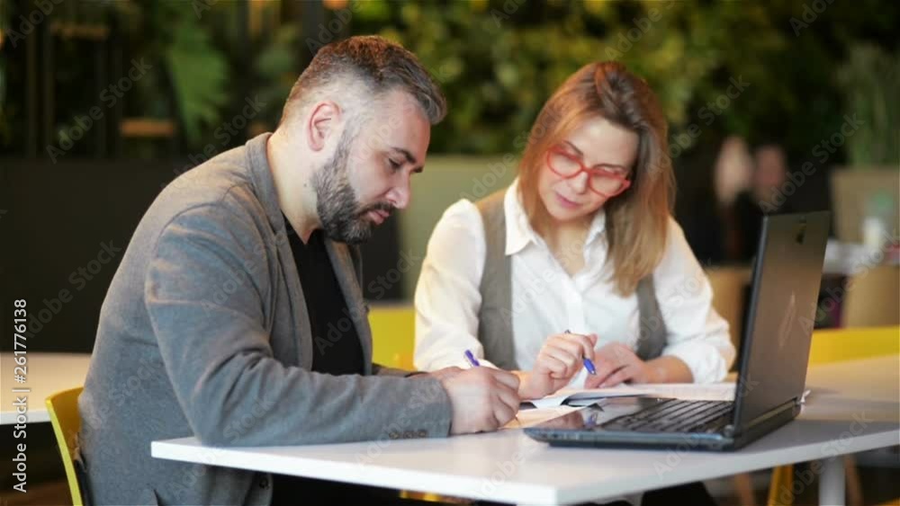 Couple of Coworkers Working Together at Office. Two Business Worker Preparing New Project on Laptop. They Write Down the Details in a Notebook. Couple of Coworkers Working Together at Office. Two Business Worker Preparing New Project on Laptop. They Write Down the Details in a Notebook.