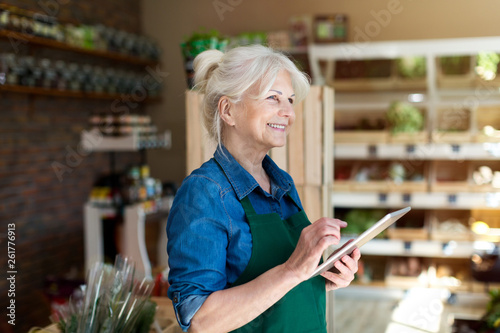 Shop assistant with digital tablet in small grocery store