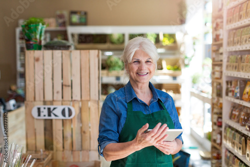 Shop assistant with digital tablet in small grocery store