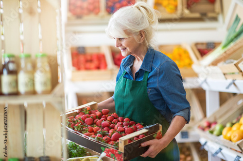 Shop assistant holding box with fresh strawberries in organic produce shop