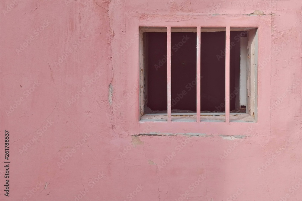 Basement window with grate on the old pink wall