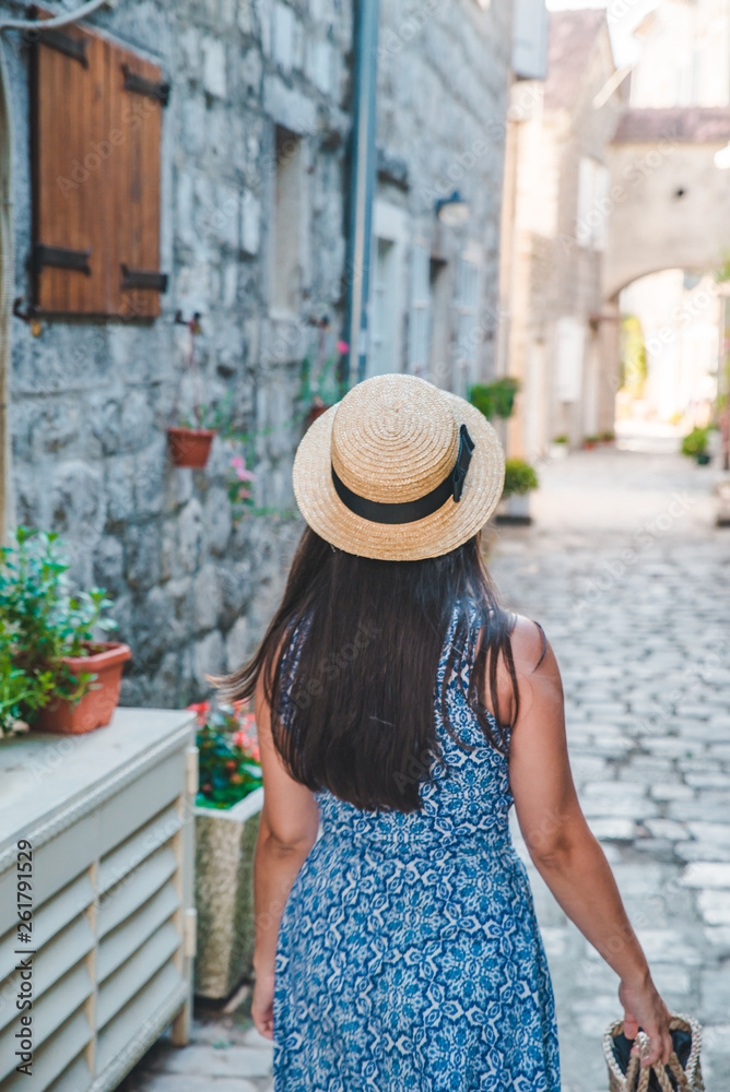 woman walking by small perast streets in hat and blue dress