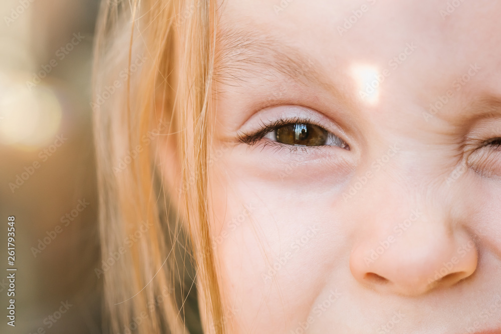 Little cute Caucasian girl with brown eyes squints in the sun, winks and makes a face. Large portrait, the eyes of a child in soft focus Little cute Caucasian girl with brown eyes squints in the sun, winks and makes a face. Large portrait, the eyes of a child in soft focus