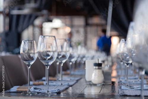 Restaurant interior  modern setting  wine and water glasses  forks and knives on textile napkins stand in row on vintage wooden table. Concept banquet  birthday  conference  group lunch