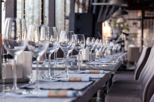 Restaurant interior, modern setting, wine and water glasses, forks and knives on textile napkins stand in row on vintage wooden table. Concept banquet, birthday, conference, group lunch