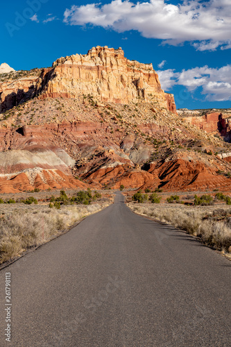 Paved road leads into the dry desert of southern Utah with mountain peak and clouds