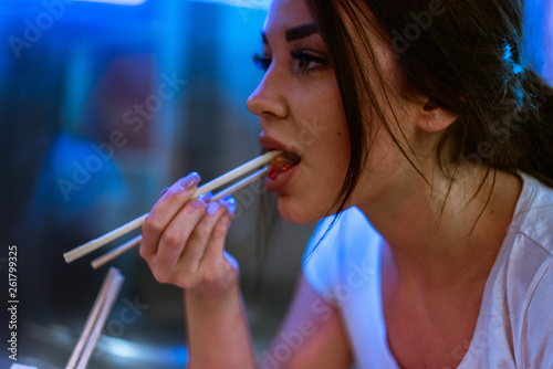 Young attractive woman eating asian food with chopsticks at cafe or restaurant.