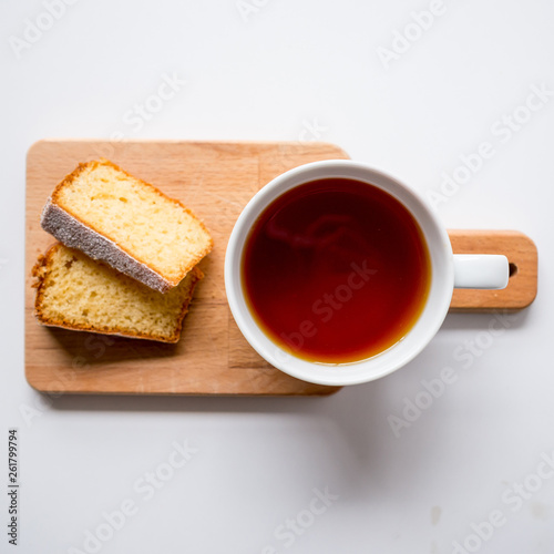 Cup of tea and two slices of sponge cake on a wooden chopping board. Top view. Squared format.