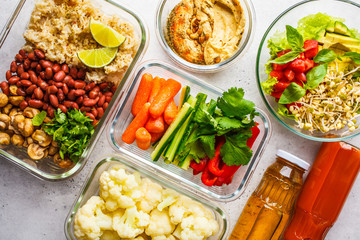 Healthy vegan food in glass containers, top view. Rice, beans, vegetables, hummus and juice.