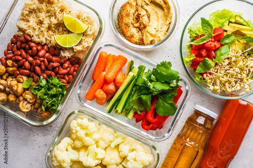 Healthy vegan food in glass containers, top view. Rice, beans, vegetables, hummus and juice.