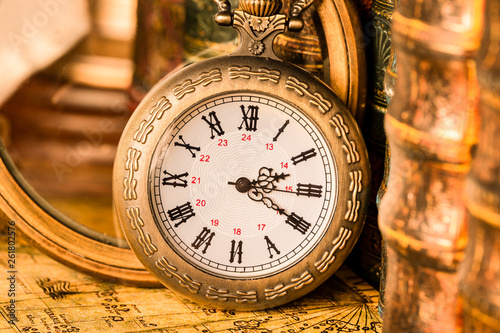 Antique clock on the background of a magnifying glass and books. Vintage style. 1565 old map of the year.