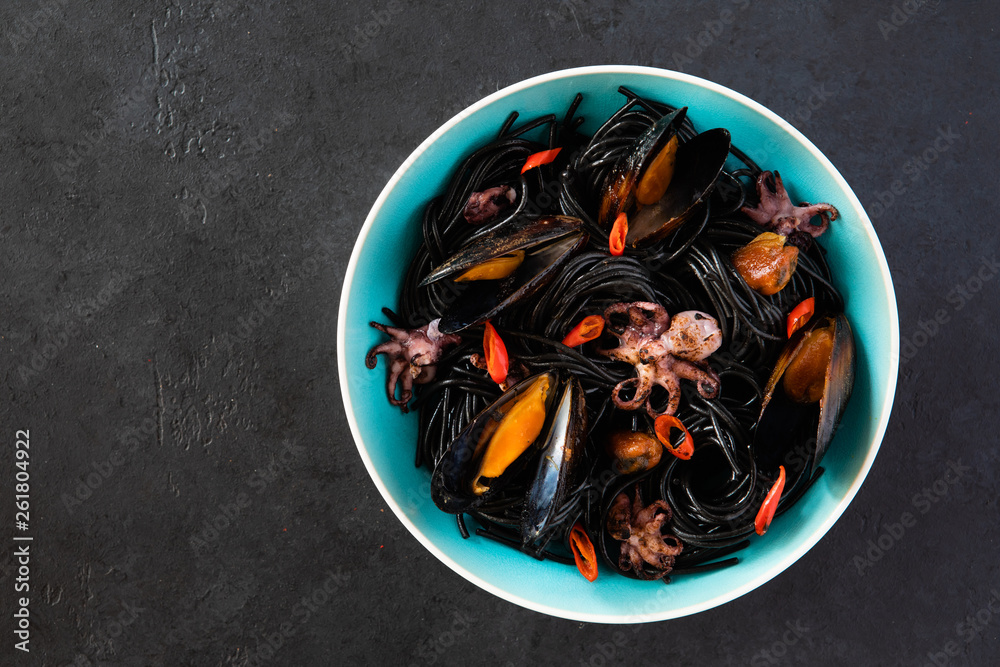 Top view of mediterranean black pasta with seafood. Spaghetti Nera with cuttlefish ink, mussels, shrimp and red chili pepper on blue plate. on dark background. Top view of mediterranean black pasta with seafood. Spaghetti Nera with cuttlefish ink, mussels, shrimp and red chili pepper on blue plate. on dark background.