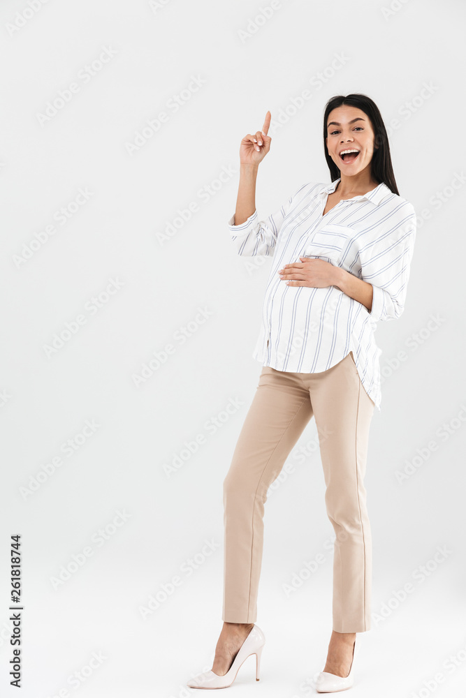 Full length photo of young pregnant businesswoman 30s smiling and touching her big tummy while standing Full length photo of young pregnant businesswoman 30s smiling and touching her big tummy while standing