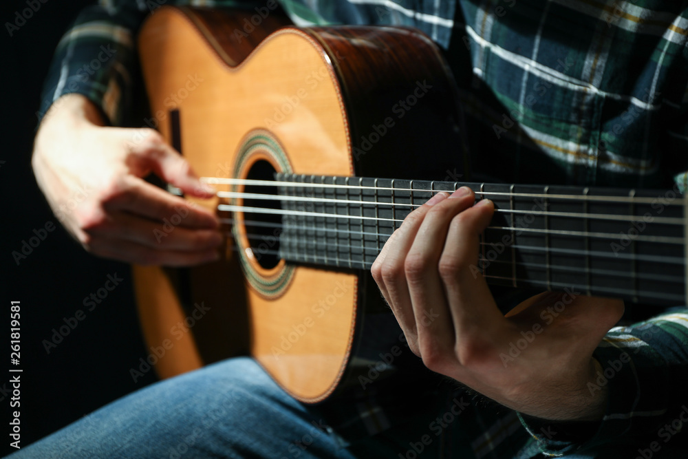 Fototapeta premium Man playing on classic guitar against dark background, closeup