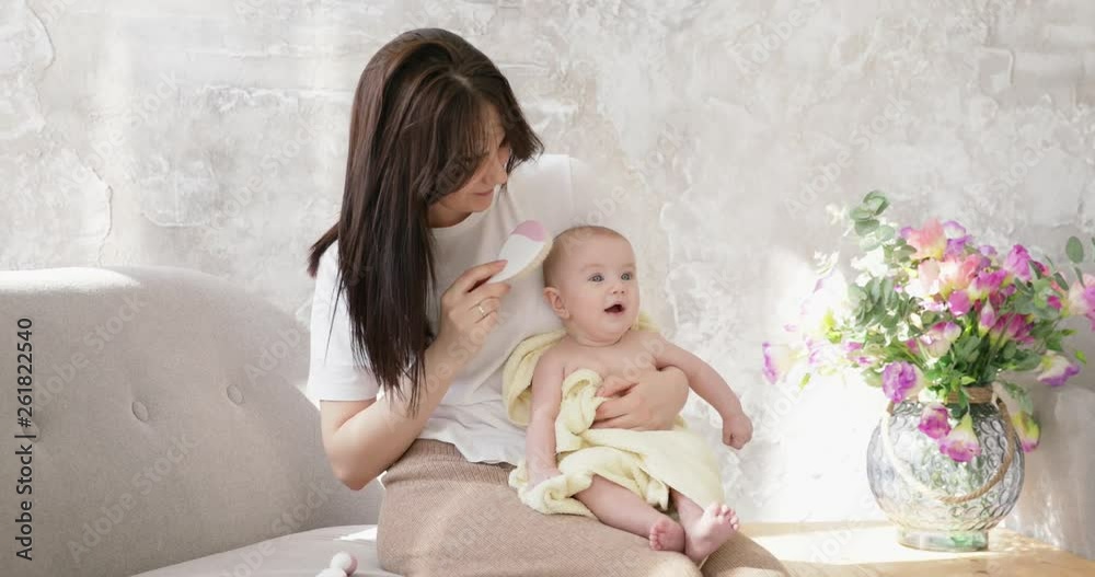 Young smiling woman combing hair baby. Mother with hairbrush. Woman holding girl wrapped in towel after bath. Young smiling woman combing hair baby. Mother with hairbrush. Woman holding girl wrapped in towel after bath.