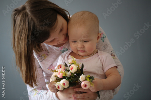 Kid girl hugging baby and holding together flowers