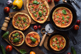 Healthy vegetarian food flatlay. Homemade rustic pizzas with tomatoes, mushrooms, eggplants and basil with raw ingredients in cast iron pans and oak boards on dark background