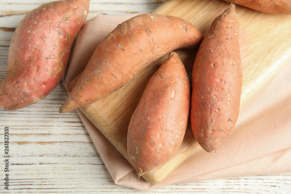Board with sweet potatoes on white wooden background