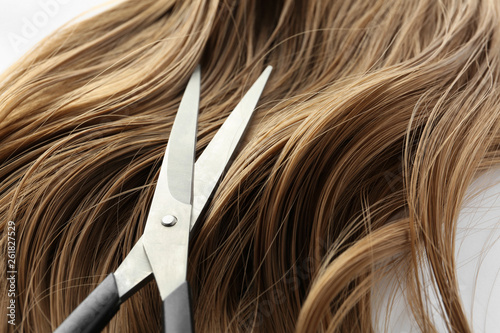 Scissors and brown wavy hair on white background, closeup. Hairdresser service
