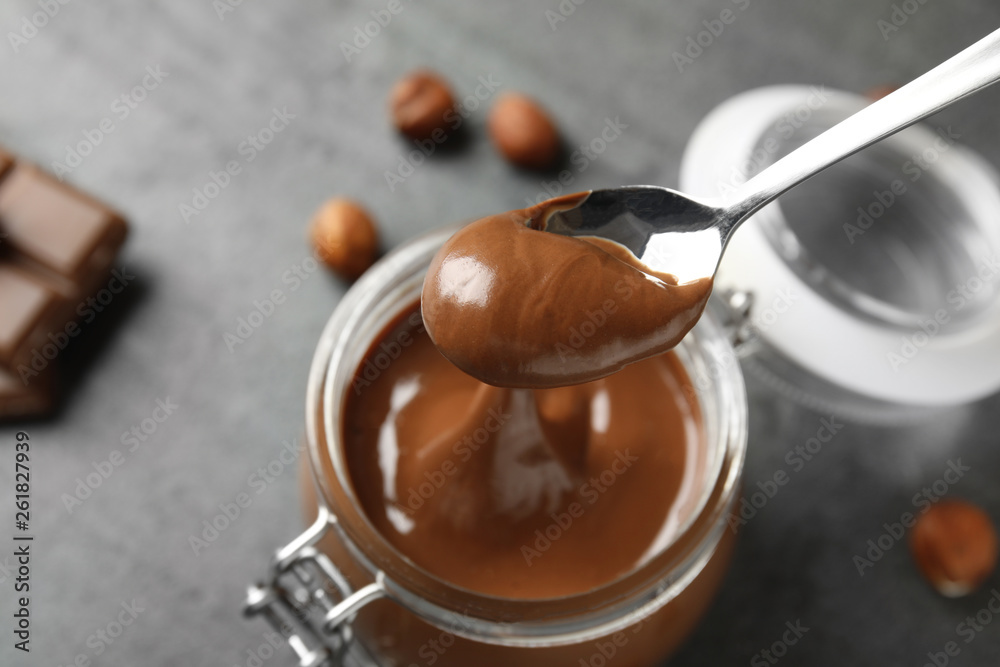 Spoon with tasty chocolate cream over full jar on table, view from above