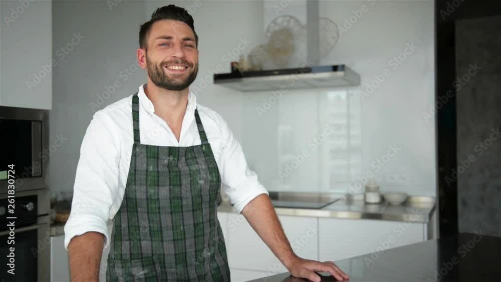 Handsome Bearded Man In Apron Posing In The Kitchen. He Looks So Happy. Handsome Bearded Man In Apron Posing In The Kitchen. He Looks So Happy.