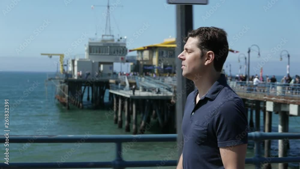 Profile side shot of man walking along a pier, birds flying around.
