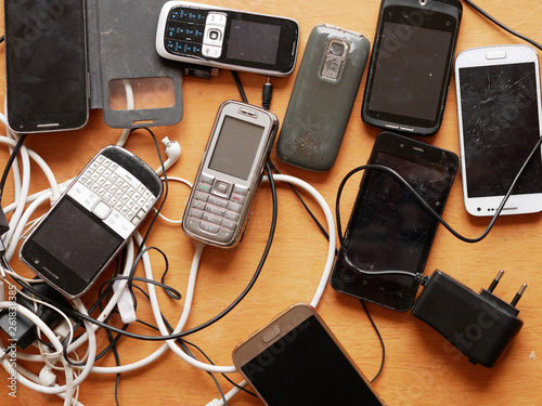 Electro waste - old and broken cell phones and cables laying on the wooden board