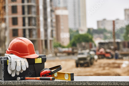 Set of safety workwear, toolbox and other professional equipment lying on stone surface against construction site. Building concept photo