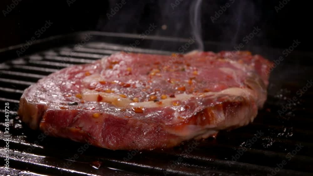 Cook presses the steak on the hot surface of the grill with a spatula on over an open fire. Cook presses the steak on the hot surface of the grill with a spatula on over an open fire.