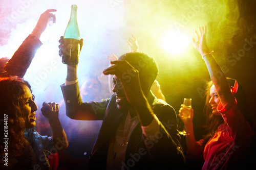 Schilderij op canvas Crowd of jovial young multiethnic clubbers dancing with raised arms in smoke and