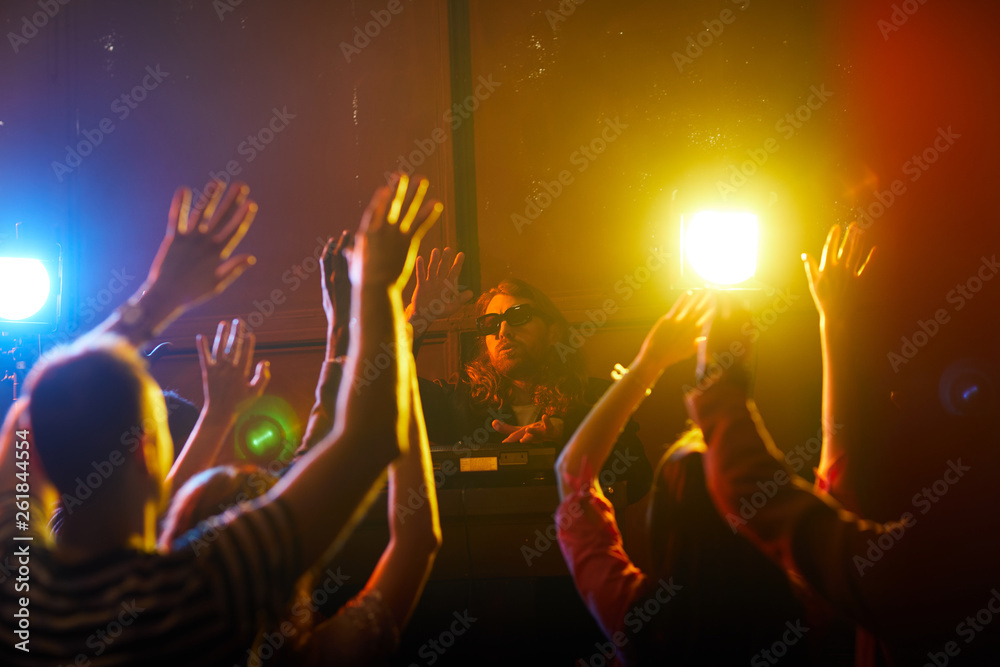 Obraz premium Brutal hipster young DJ in sunglasses twisting disc and waving hand together with crowd at party in nightclub
